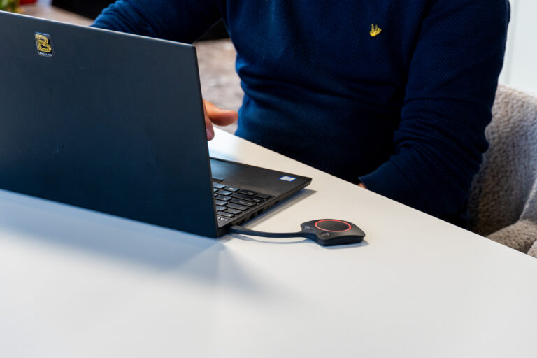 Barco Clickshare dongel, geplugd in een laptop die op een vergadertafel staat.
