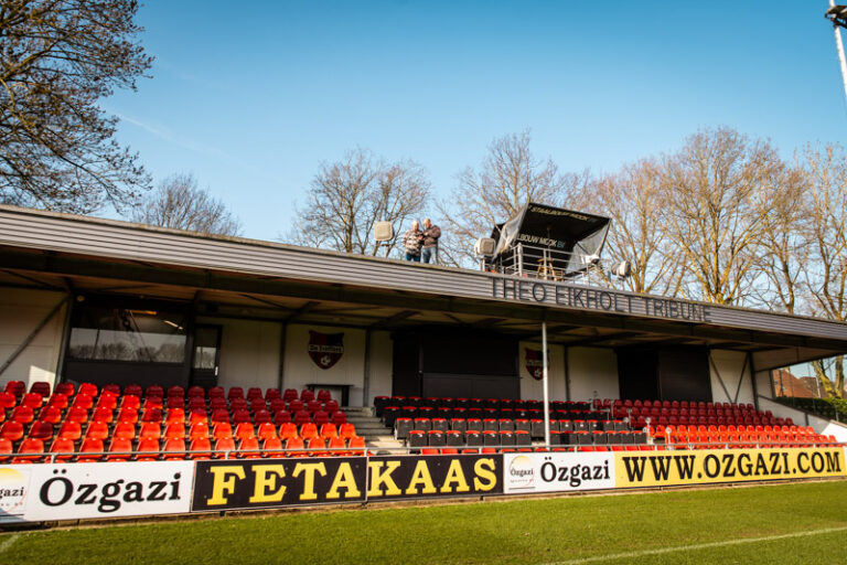 Tribune van voetbalvereniging de Treffers, met op het dak 2 mannen die op een tablet kijken voor het afstemmen van de nieuwe geluidsinstallatie.