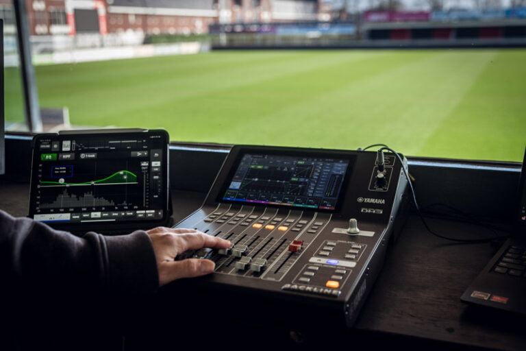 Mengpaneel in de ruimte van de live omroeper, met uitzicht op het groene voetbalveld.