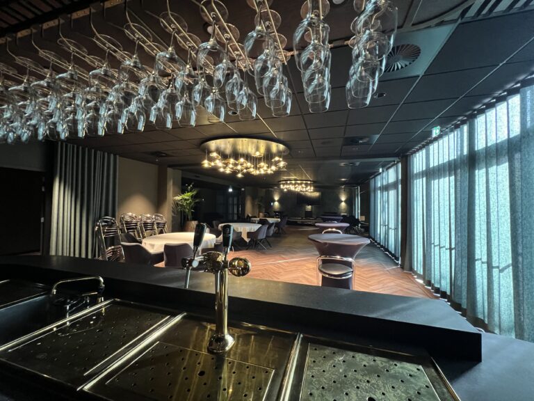 Stijlvolle vergader- en conferentiezaal van Kasteel Eyckholt, gezien van uit de bar. In de ruimte staan chic beklede hangtafels en hangen sfeervolle kroonluchters.